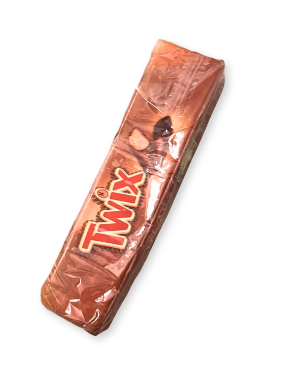 „Miękki Butter Squishy w kształcie batonika Twix. Złoto-brązowa kolorystyka i nadruk inspirowany opakowaniem słodyczy. Podłużny kształt, zaokrąglone krawędzie i wygląd czekoladowego batonika.”